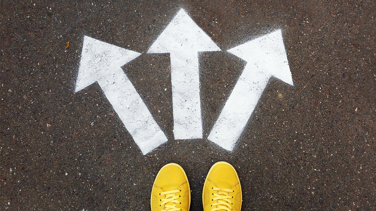 Three arrows sprayed onto a road pointing away from a pair of feet